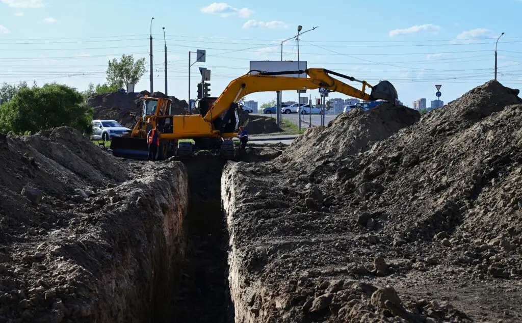Excavator trenching near urban road — earthmoving and utility installation preparation